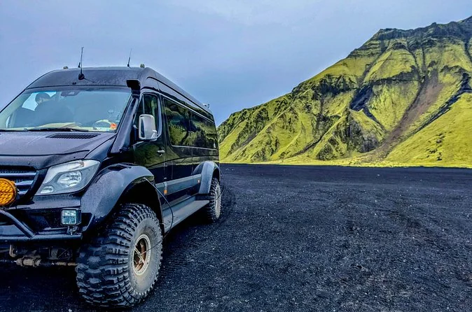 Una furgoneta 4x4 negra sobre arena negra con una montaña verde al fondo